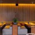 An elegant restaurant setting with moody lighting and modern seating arrangements. A wooden wall divides the room.