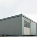 A mobile building complex is completed at a construction site. A bulldozer is visible in the distance.