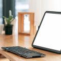 A portable tablet with a blank screen and black keyboard set in front of it on a wooden desk, all in a room with bright windows.