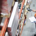A top-down view of a man in an orange vest taking inventory of items in a warehouse with a handheld device.