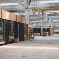 A wide shot of a warehouse with concrete flooring with various modular buildings set up throughout the space.