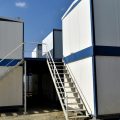 Stacked white modular buildings with staircases leading up to higher levels and bliue trim around the edges.