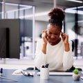 A woman sitting at an office desk putting her fingers up to her temples as if she has a headache.