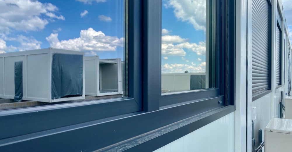 A close-up on the windows of a trailer office showing the reflection of several other modular buildings in the background.