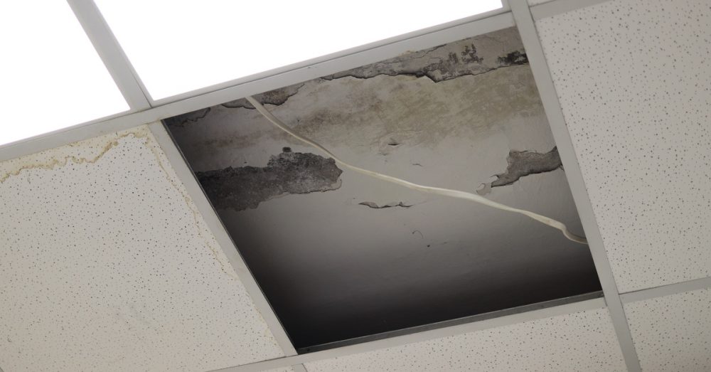 A close-up of a ceiling tile fallen out of place and water damage causing damage to the exposed ceiling.