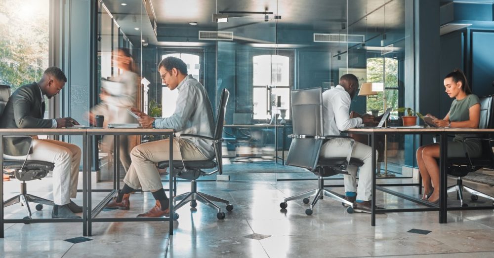 An office with professional employees at their desks Natural light pours in through glass walls and windows