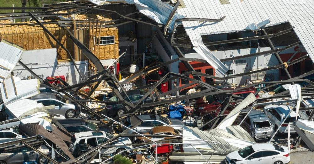 A natural disaster has destroyed two buildings. The roof has blown away, cars are damaged, and debris is scattered.