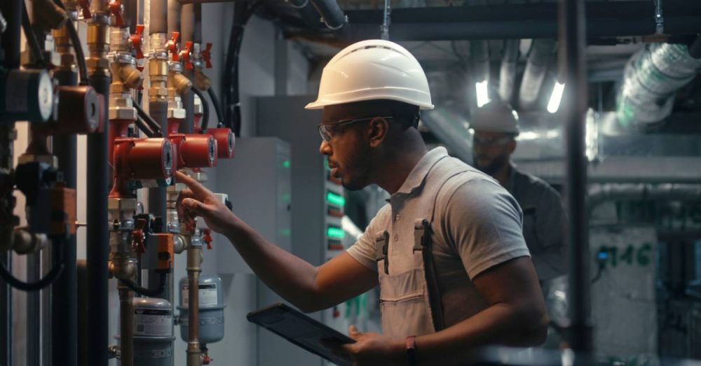 An inspector wearing a safety uniform and protective helmet closely inspects the pipeline system in an industrial plant.