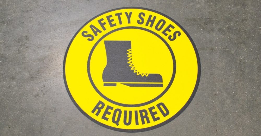 A yellow warning sign signaling to employees that they should wear safety shoes on the industrial work floor.